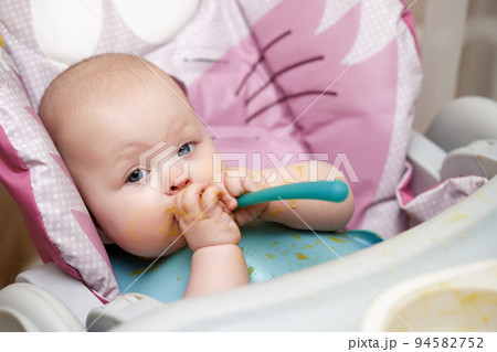 baby girl eating with spoon in kitchen baby girl eating with spoon in kitchen 94582752