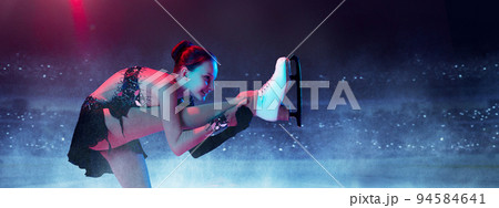 Base program element. Young female figure skater in show dress performing short program at ice arena background. Dance, winter sports, achievements, champion concept 94584641