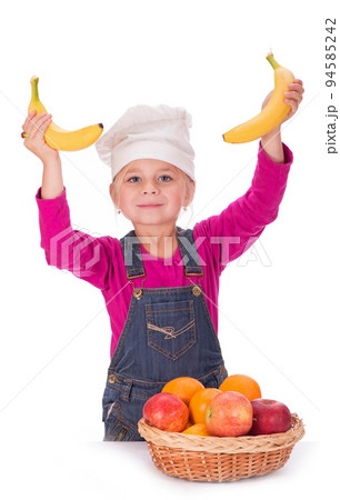 Close-up portrait of a little girl holding fruits - apples, bananas and oranges. Isolated on a light background. 94585242