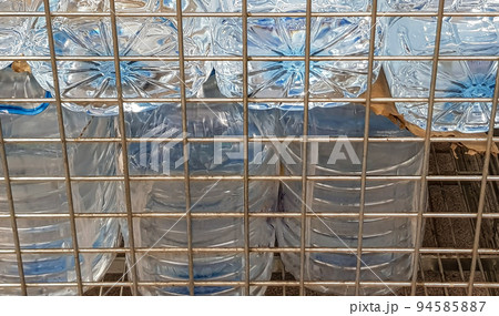 Storage and transportation of large plastic bottles for clean drinking water in a container with a metal grate, close-up Storage and transportation of large plastic bottles for clean drinking water in a container with a metal grate, close-up 94585887