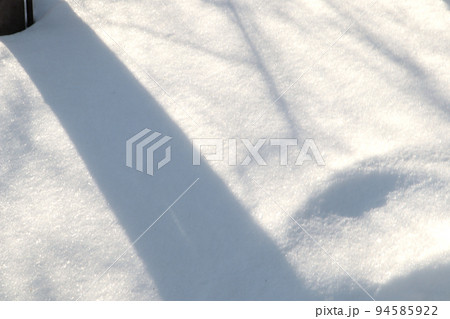 On a sunny winter day, natural shadows from trees form on the snow surface, an abstract pattern 94585922