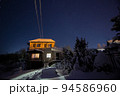 Night shot of a countryside brick house with lighted windows with a starry sky on a background in winter. Concept of peace, magic, idyllic, home, dreams. 94586960