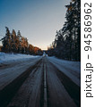 Country snowy road through coniferous forest in winter. Sunset 94586962