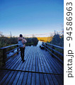 Young woman standing on a wooden pier and taking photo of a large crayfish lake. State Natural Reserve Cancer Lakes , St. Petersburg 94586963