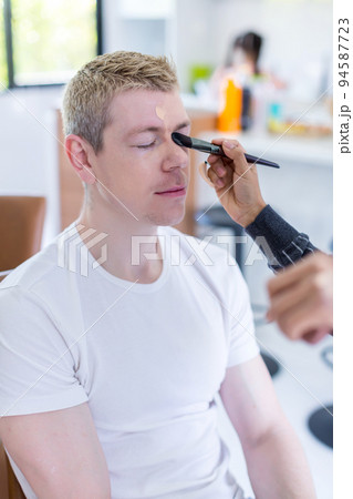 Stylist is putting make up on man.	 94587723
