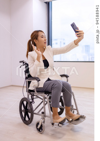 Office workers woman on a wheelchair in bright office and holding smart phone. 94588941