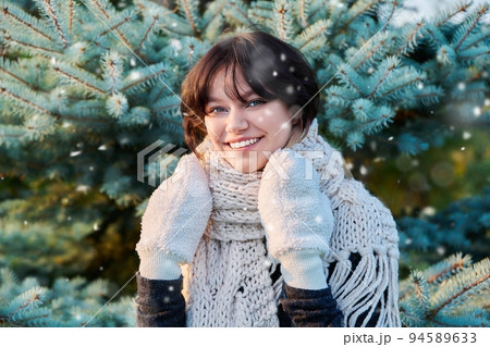 Portrait of young woman in knitted scarf mittens in winter, near Christmas tree Portrait of young woman in knitted scarf mittens in winter, near Christmas tree 94589633