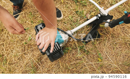 Gardener man hand starting gas lawn trimmer. Hands of a professional lawn mower. 94590116