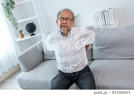 An agonizing senior man is holding his back due to back pain. An agonizing senior man is holding his back due to back pain. 94590605