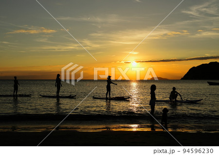 夕暮れの逗子海岸、陽射しを浴びてSUPヨガを楽しむ若者たちと犬の散歩をする女の子 94596230