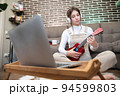 Beautiful young hipster girl in casual clothes learning to play the ukulele guitar while sitting on the floor in the living room at home, hobby leisure time concept 94599803