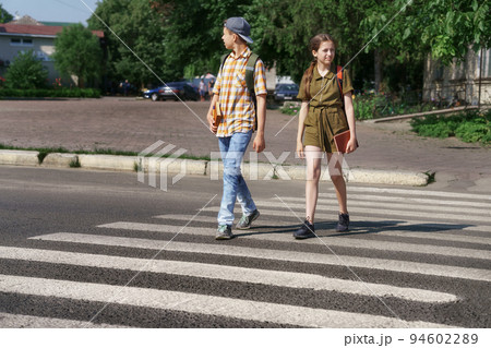 teenage schoolchildren, a boy and a girl cross the road at a pedestrian crossing teenage schoolchildren, a boy and a girl cross the road at a pedestrian crossing 94602289