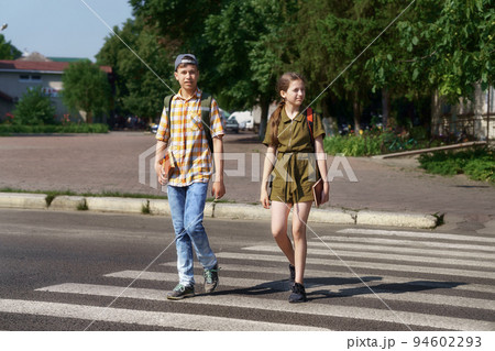 teenage schoolchildren, a boy and a girl cross the road at a pedestrian crossing teenage schoolchildren, a boy and a girl cross the road at a pedestrian crossing 94602293