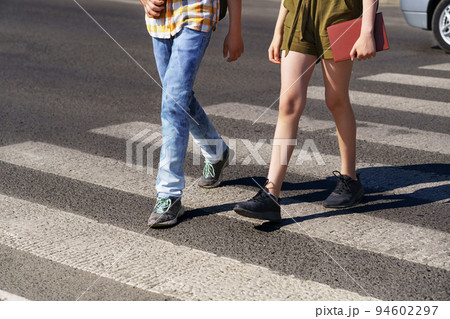 teenage schoolchildren, a boy and a girl cross the road at a pedestrian crossing teenage schoolchildren, a boy and a girl cross the road at a pedestrian crossing 94602297