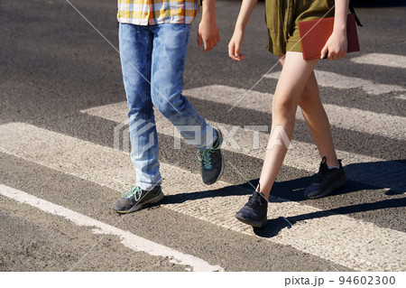 teenage schoolchildren, a boy and a girl cross the road at a pedestrian crossing 94602300