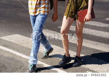 teenage schoolchildren, a boy and a girl cross the road at a pedestrian crossing teenage schoolchildren, a boy and a girl cross the road at a pedestrian crossing 94602302
