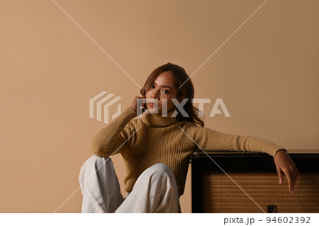 Portrait of fashionable woman wearing trendy sweater sitting near vintage radio, studio shot on beige background Portrait of fashionable woman wearing trendy sweater sitting near vintage radio, studio shot on beige background 94602392