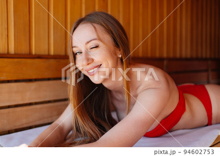 woman in a red swimsuit lies on a bench in the sauna.  94602753