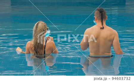The loving couple hugs and kisses, drinking blue cocktail alcohol liquor in swimming pool at hotel outdoor. Portrait of caucasian man and woman. 94603732