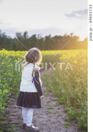 girl with Ukrainian ribbons in her hair in a flowering field at sunset 94603733