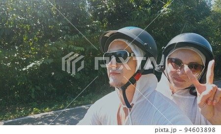 Two caucasian tourist woman man drive on red scooter. Make it selfie. Love couple on motorbike in white clothes to go on forest road trail trip. Two caucasian tourist woman man drive on red scooter. Make it selfie. Love couple on motorbike in white clothes to go on forest road trail trip. 94603898