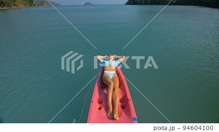 Pretty slim woman in elegant swimsuit lies in pink plastic kayak drifting on azure ocean at exotic resort upper view. 94604100