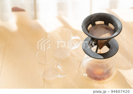 【日本】朝日が差し込む窓際の床に置かれたコーヒーサーバーとグラスとドリッパーに入った粗挽きコーヒー豆 【日本】朝日が差し込む窓際の床に置かれたコーヒーサーバーとグラスとドリッパーに入った粗挽きコーヒー豆 94607420