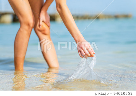 A female volunteer picks up plastic plastic on the ocean shore A female volunteer picks up plastic plastic on the ocean shore 94610555