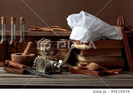 Chef's hat, vintage cookbooks, and old kitchen utensils on the kitchen table. Chef's hat, vintage cookbooks, and old kitchen utensils on the kitchen table. 94610649