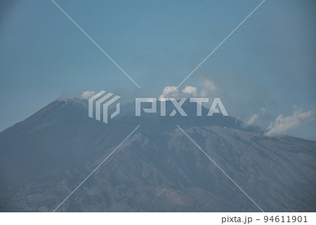 View of famous volcanic Mount Etna emitting smoke. Scenic tourist attraction with blue sky in background. Majestic mountains with dramatic landscape during summer. View of famous volcanic Mount Etna emitting smoke. Scenic tourist attraction with blue sky in background. Majestic mountains with dramatic landscape during summer. 94611901