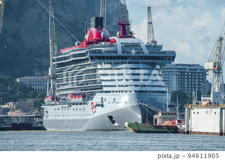 Luxurious large cruise ship moored at harbor with mountain and sky in background. Majestic nautical vessel at Mediterranean port in ancient city. View of boats and town at coastline. 94611905