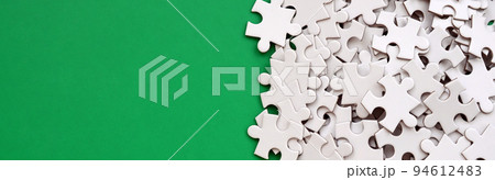 A pile of uncombed elements of a white jigsaw puzzle lies on the background of a green surface. Texture photo with copy space for text 94612483