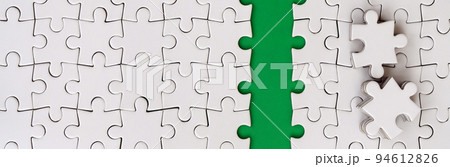The green path is laid on the platform of a white folded jigsaw puzzle. The missing elements of the puzzle are stacked nearby. Texture image with space for text 94612826