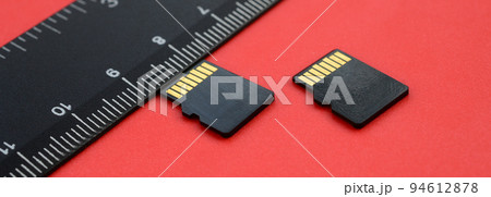 Two small micro SD memory cards lie on a red background next to a black ruler. A small and compact data and information store Two small micro SD memory cards lie on a red background next to a black ruler. A small and compact data and information store 94612878