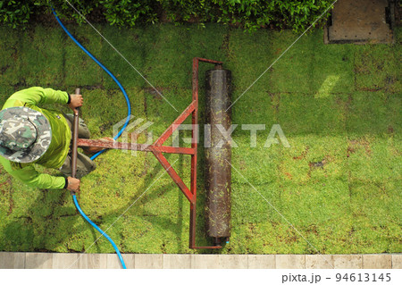 Top view worker pushes the heavy steel drum on the grass field during growing process 94613145