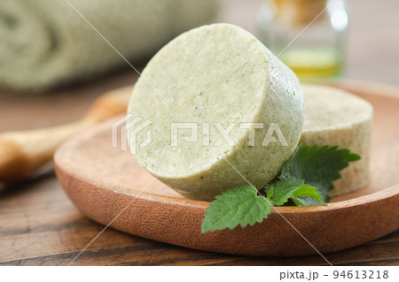 Nettle solid shampoo pieces or homemade natural organic soap bars on wooden soap dish, fresh green nettle leaves. A bath towel, essential oil bottle and comb on background. Selective focus. Nettle solid shampoo pieces or homemade natural organic soap bars on wooden soap dish, fresh green nettle leaves. A bath towel, essential oil bottle and comb on background. Selective focus. 94613218