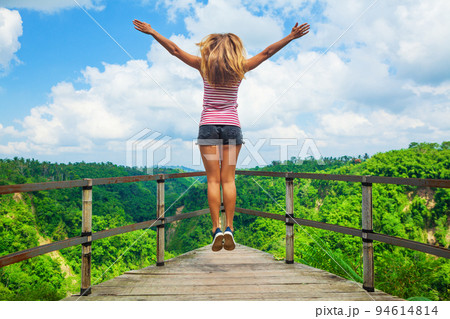 Woman stand at balcony on high cliff with jungle view Woman stand at balcony on high cliff with jungle view 94614814