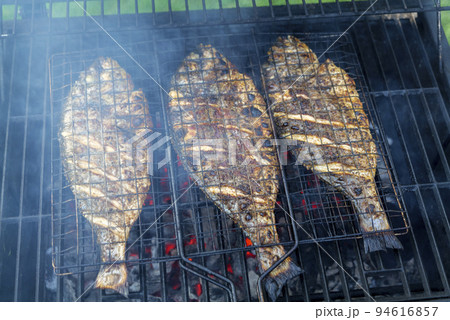 Grilling process of dorado fish on a charcoal BBQ grill in the backyard 94616857