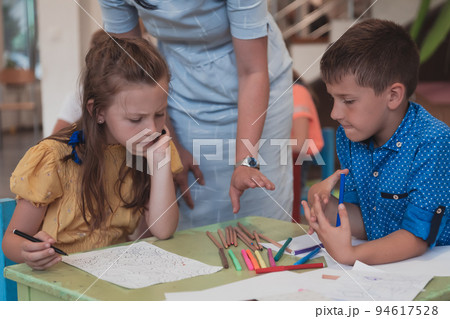Creative kids during an art class in a daycare center or elementary school classroom drawing with female teacher. Creative kids during an art class in a daycare center or elementary school classroom drawing with female teacher. 94617528