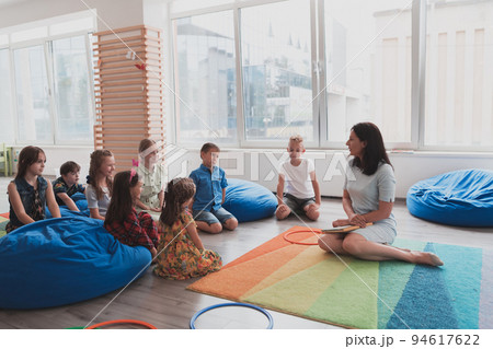 A happy female teacher sitting and playing hand games with a group of little schoolchildren A happy female teacher sitting and playing hand games with a group of little schoolchildren 94617622