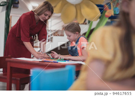 Creative kids during an art class in a daycare center or elementary school classroom drawing with female teacher.  94617655