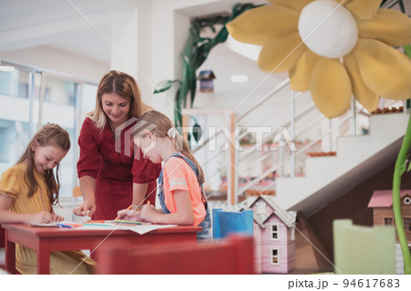 Creative kids during an art class in a daycare center or elementary school classroom drawing with female teacher. Creative kids during an art class in a daycare center or elementary school classroom drawing with female teacher. 94617683