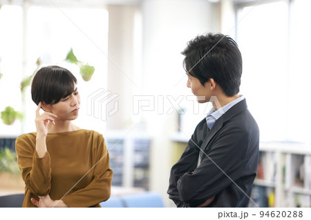 打ち合わせ_頭に指を当て困った表情の女性と腕組みして話す男性1 94620288