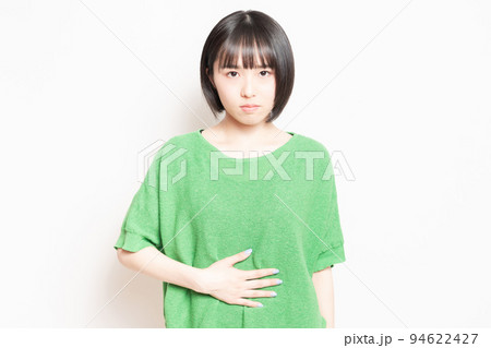 白背景の前で、お腹を手で抑える若い女性 94622427