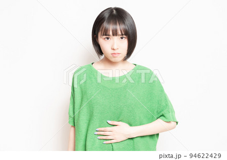 白背景の前で、お腹を手で抑える若い女性 白背景の前で、お腹を手で抑える若い女性 94622429
