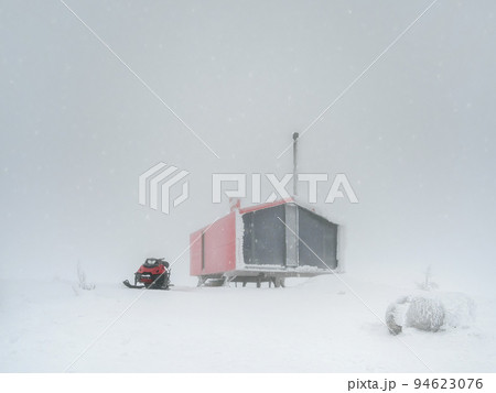 Poor visibility in snowfall. Frozen house. Red house and a snowmobile on a foggy snow-covered mountain. Winter holidays, extreme adventures in winter. 94623076