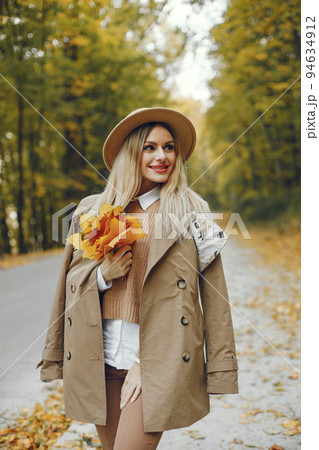 Woman posing for a photo in the autumn park. Caucasian girl has red lips. Woman wearing beige coat and a hat. Woman posing for a photo in the autumn park. Caucasian girl has red lips. Woman wearing beige coat and a hat. 94634912