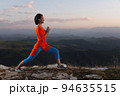 young girl is doing yoga and fitness outdoors in a beautiful mountain landscape. Sunset light, warrior pose 94635515