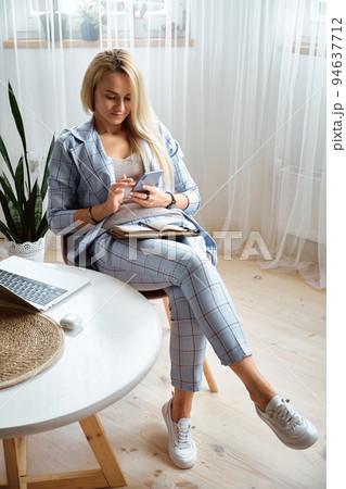 Young woman using mobile phone sitting at home office desk, remote work at home Young woman using mobile phone sitting at home office desk, remote work at home 94637712