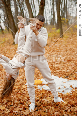 Man and her little girl playing in autumn forest and laughing. Brunette man holding his daughter upside down. Family wearing beige sportive costumes. Man and her little girl playing in autumn forest and laughing. Brunette man holding his daughter upside down. Family wearing beige sportive costumes. 94638120